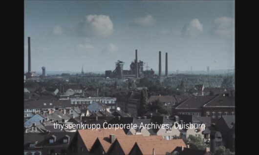 A cityscape with rows of houses in the foreground and a large industrial complex with smokestacks in the distance under a blue sky. Text reads: thyssenkrupp Corporate Archives, Duisburg.